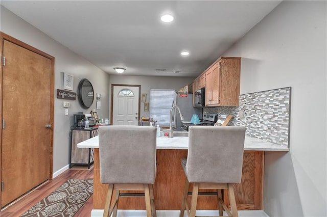 kitchen featuring kitchen peninsula, tasteful backsplash, hardwood / wood-style flooring, and a kitchen breakfast bar