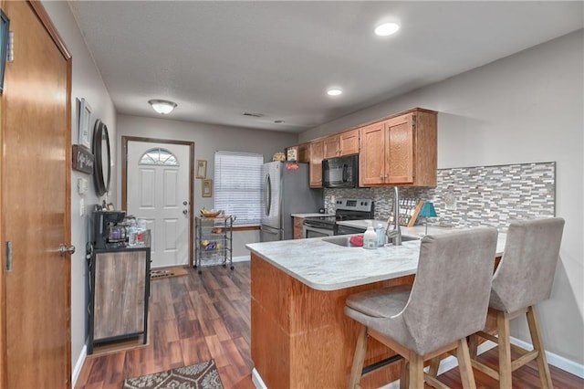 kitchen with backsplash, appliances with stainless steel finishes, a kitchen breakfast bar, dark wood-type flooring, and kitchen peninsula