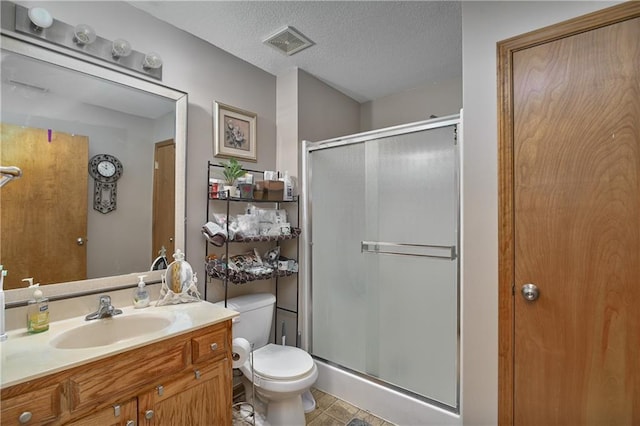 bathroom featuring vanity, a textured ceiling, toilet, and a shower with door