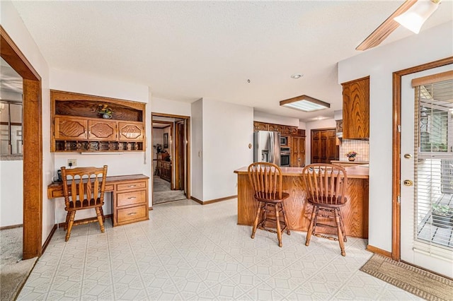 kitchen with built in desk, kitchen peninsula, backsplash, a breakfast bar, and appliances with stainless steel finishes