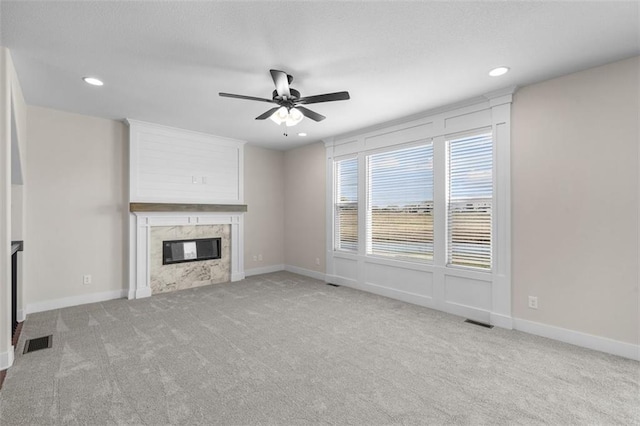 unfurnished living room with a high end fireplace, light carpet, and ceiling fan