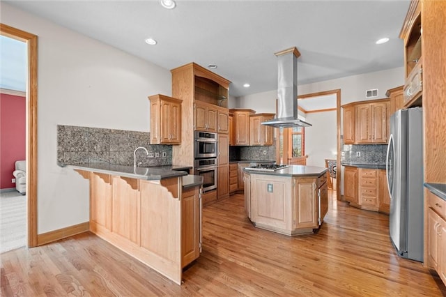 kitchen featuring kitchen peninsula, island exhaust hood, appliances with stainless steel finishes, a kitchen island, and light wood-type flooring