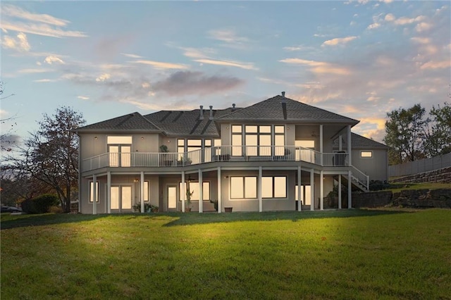 back house at dusk featuring a yard and a balcony