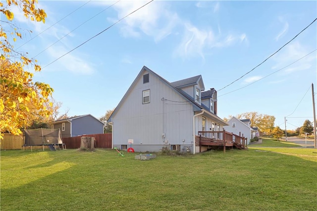 back of property with a trampoline, a wooden deck, and a lawn