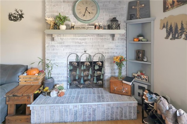 living room featuring built in shelves, hardwood / wood-style floors, and a brick fireplace