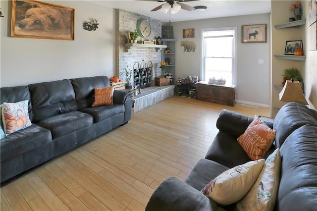 living room featuring ceiling fan, a brick fireplace, and light wood-type flooring