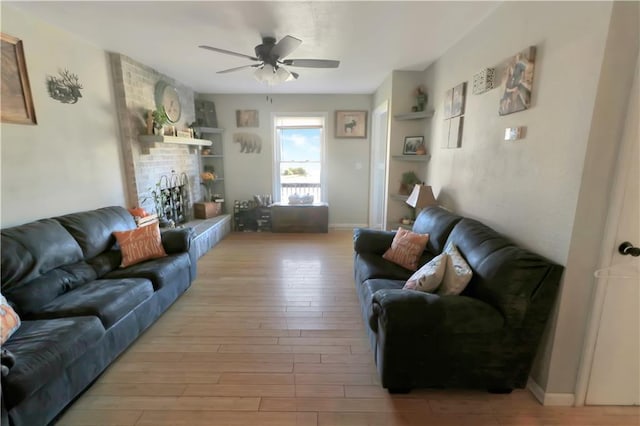 living room with a brick fireplace, built in shelves, light hardwood / wood-style flooring, and ceiling fan