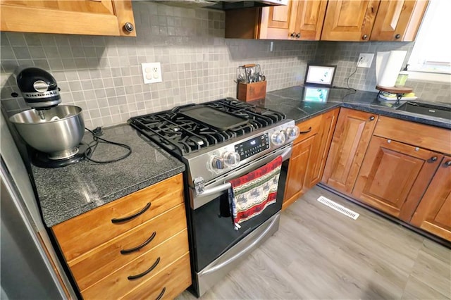 kitchen featuring tasteful backsplash, stainless steel range with gas stovetop, light wood-type flooring, and dark stone countertops