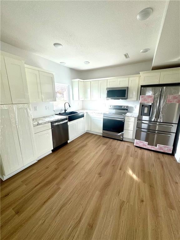 kitchen with sink, white cabinetry, stainless steel appliances, and light wood-type flooring