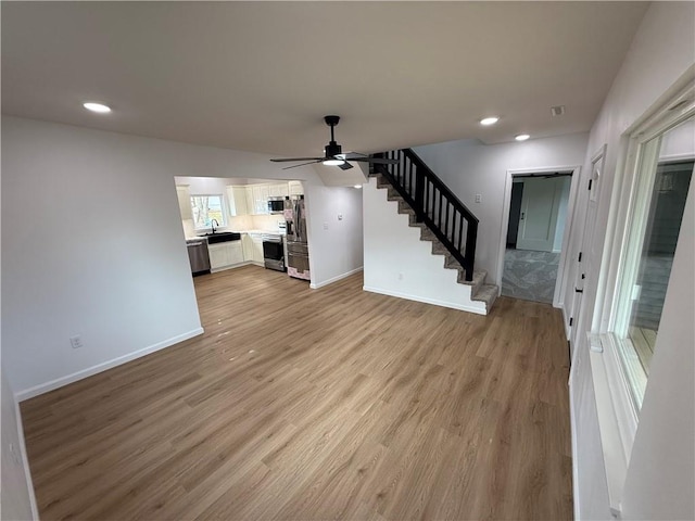 unfurnished living room featuring ceiling fan, sink, and light wood-type flooring