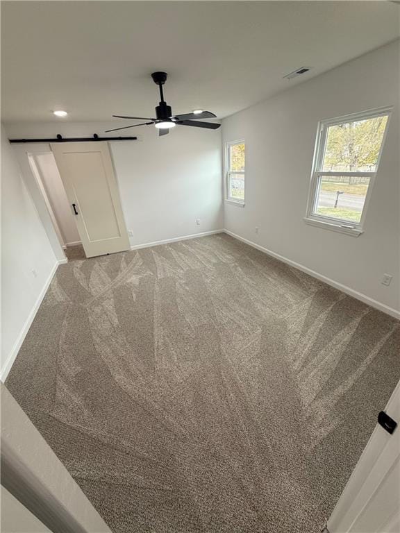 unfurnished room featuring a wealth of natural light, a barn door, and carpet floors