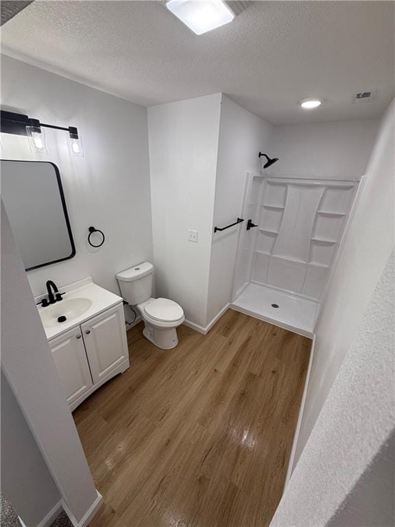 bathroom featuring wood-type flooring, a textured ceiling, toilet, walk in shower, and vanity