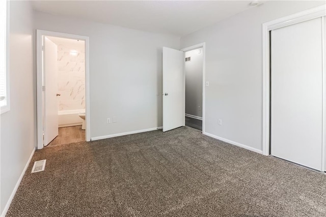 unfurnished bedroom with a closet, ensuite bath, and dark carpet