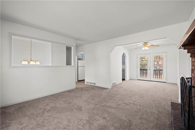 unfurnished living room with carpet flooring, french doors, ceiling fan with notable chandelier, and a fireplace