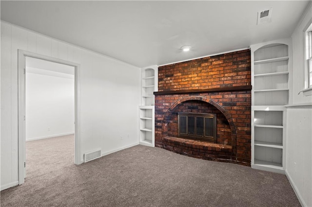 unfurnished living room with carpet, a brick fireplace, built in features, and wood walls