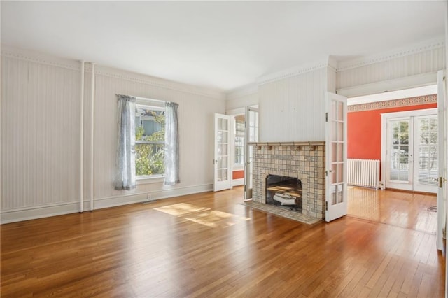 unfurnished living room with a tile fireplace, french doors, ornamental molding, and hardwood / wood-style flooring