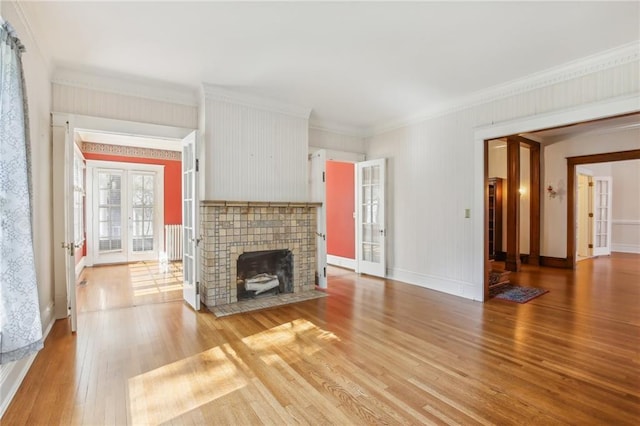 unfurnished living room with hardwood / wood-style flooring, a fireplace, crown molding, and french doors