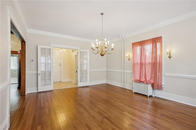 empty room featuring radiator, an inviting chandelier, french doors, ornamental molding, and wood-type flooring