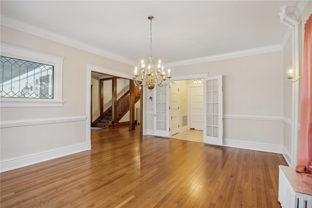 unfurnished dining area featuring crown molding, french doors, wood-type flooring, and an inviting chandelier