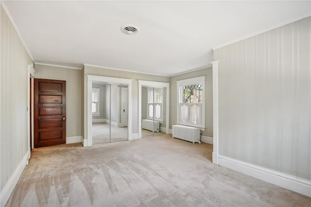 unfurnished bedroom featuring two closets, light colored carpet, radiator, and crown molding