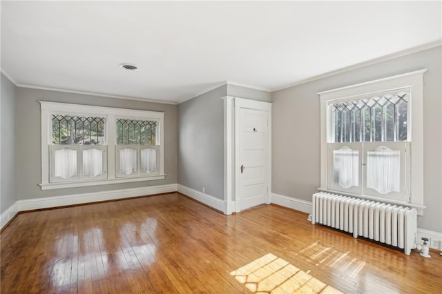 spare room featuring light hardwood / wood-style floors, a healthy amount of sunlight, radiator heating unit, and crown molding