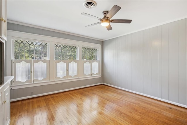 spare room with ceiling fan, wooden walls, ornamental molding, and light wood-type flooring