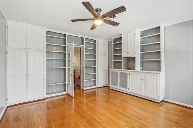 unfurnished living room featuring ceiling fan, light hardwood / wood-style flooring, and wooden walls