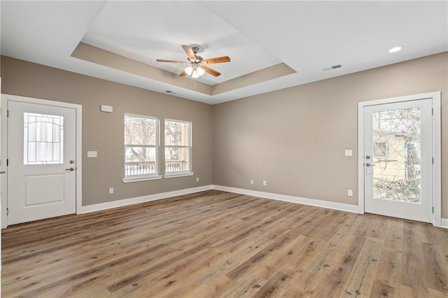 foyer with a raised ceiling, ceiling fan, a wealth of natural light, and light wood-type flooring