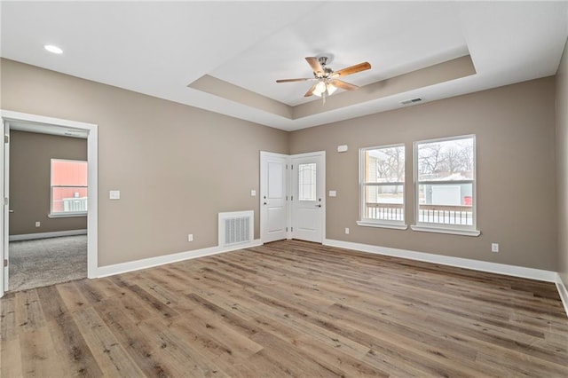 unfurnished room with ceiling fan, a tray ceiling, and light wood-type flooring