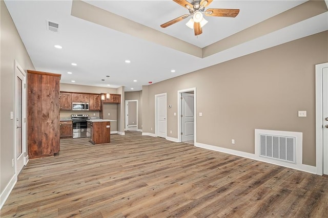 kitchen featuring a center island, light wood-type flooring, appliances with stainless steel finishes, a kitchen breakfast bar, and ceiling fan