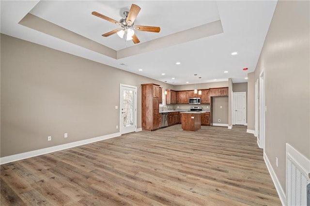 kitchen featuring pendant lighting, light hardwood / wood-style flooring, appliances with stainless steel finishes, a center island, and a tray ceiling