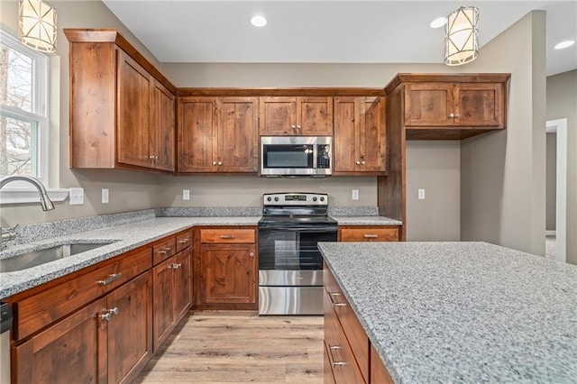 kitchen featuring sink, light hardwood / wood-style flooring, appliances with stainless steel finishes, hanging light fixtures, and light stone countertops