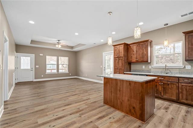 kitchen with sink, hanging light fixtures, a center island, light stone counters, and a raised ceiling