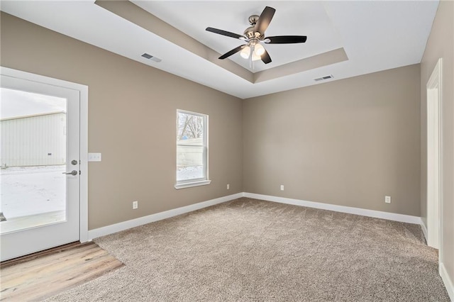 carpeted spare room featuring a raised ceiling and ceiling fan