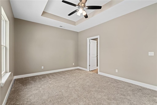 spare room featuring ceiling fan, light colored carpet, and a tray ceiling