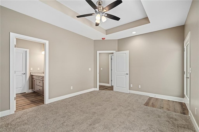 unfurnished bedroom featuring ensuite bathroom, carpet floors, ceiling fan, and a tray ceiling