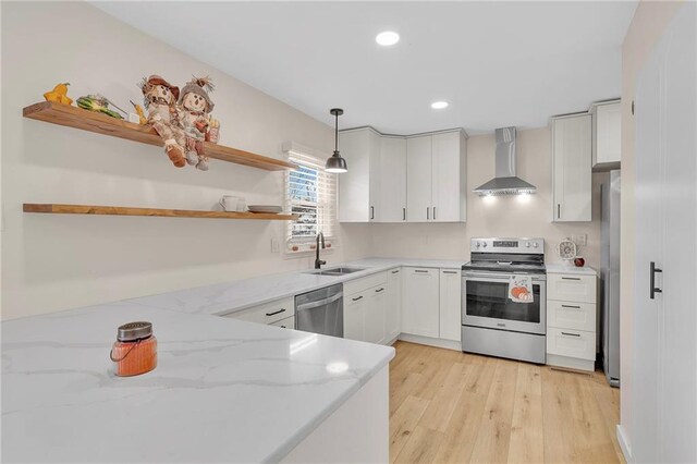 kitchen featuring wall chimney range hood, light stone counters, white cabinetry, stainless steel appliances, and decorative light fixtures