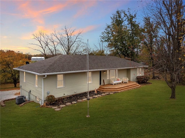 back house at dusk with a wooden deck, a lawn, and central AC unit