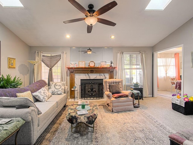 living room with lofted ceiling with skylight, a tiled fireplace, carpet flooring, and ceiling fan