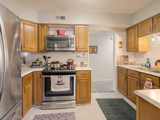 kitchen featuring sink, backsplash, a textured ceiling, stainless steel appliances, and light tile patterned floors