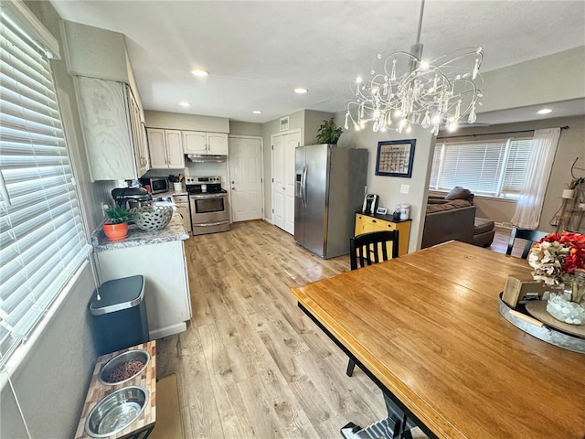 kitchen featuring light hardwood / wood-style floors, a notable chandelier, pendant lighting, appliances with stainless steel finishes, and white cabinetry