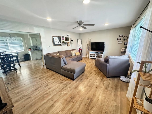 living room with ceiling fan with notable chandelier, plenty of natural light, and light hardwood / wood-style flooring