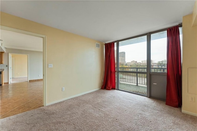 carpeted spare room featuring floor to ceiling windows, baseboards, and tile patterned floors
