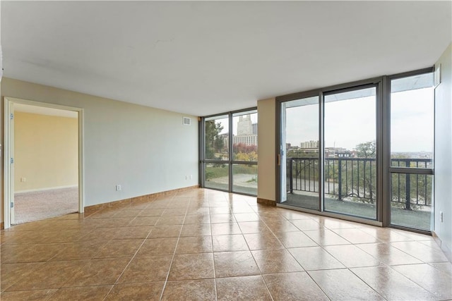 spare room with floor to ceiling windows, healthy amount of natural light, tile patterned flooring, and baseboards