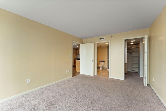 unfurnished bedroom featuring a walk in closet, a closet, and light colored carpet