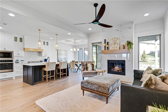 living room with a tile fireplace, ceiling fan with notable chandelier, and light wood-type flooring