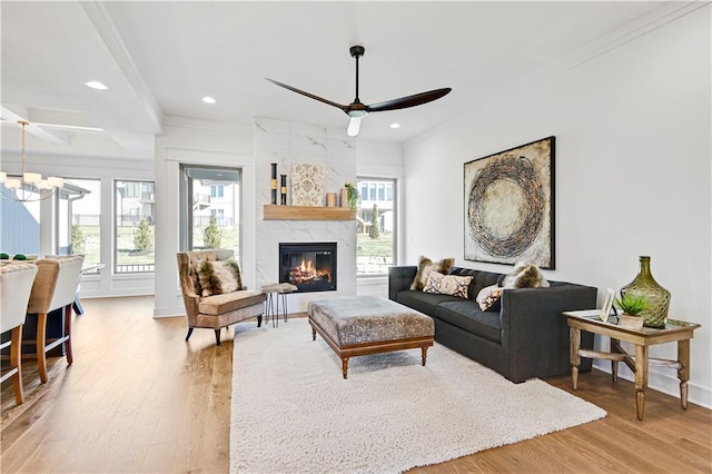 living room featuring hardwood / wood-style floors, ceiling fan with notable chandelier, ornamental molding, and a fireplace