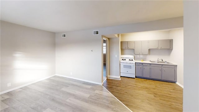 kitchen featuring sink, gray cabinetry, light wood-type flooring, and white range oven