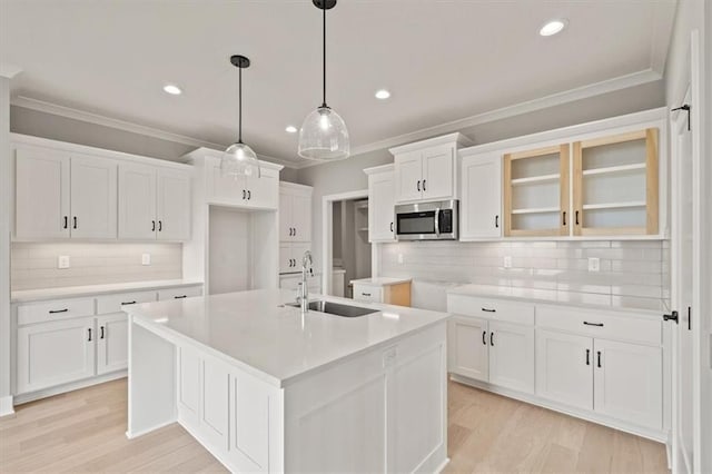 kitchen with sink, hanging light fixtures, decorative backsplash, a center island with sink, and white cabinets