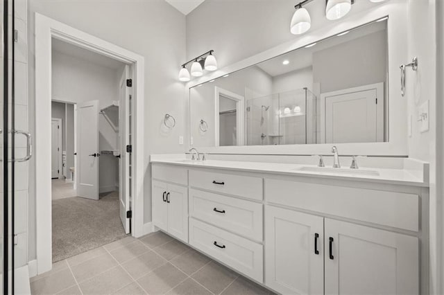 bathroom with a stall shower, double vanity, tile patterned flooring, a spacious closet, and baseboards